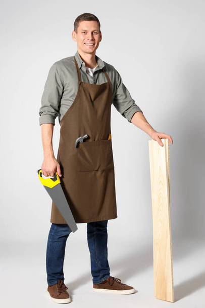 Handsome carpenter with wooden planks and hand saw on light grey - Photo, Image
