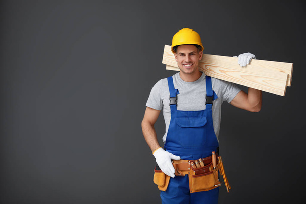Handsome carpenter with wooden planks on dark background. Space  - Photo, image