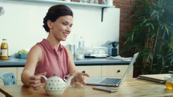 Woman pouring tea into cup during video call. Girl using laptop for video chat. - Záběry, video