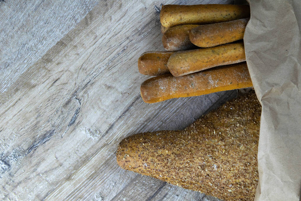 Different types of fresh bread in a craft bag stand on a wooden table. - Photo, Image