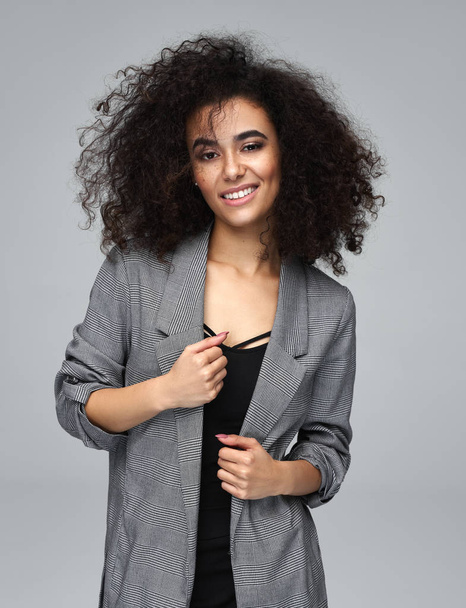 Mujer alegre latinoamericana con peinado afro desgaste chaqueta gris aislado sobre fondo gris
 - Foto, Imagen