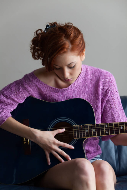 giovane donna con i capelli lunghi seduta sul pavimento con chitarra acustica - Foto, immagini