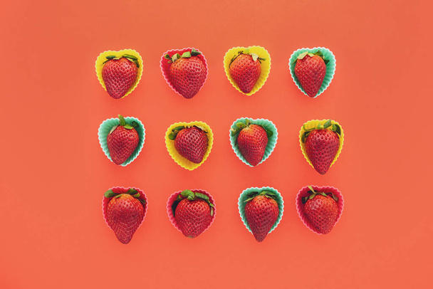 Φράουλες σε πολύχρωμο σχήμα καρδιάς πλαστικά καλούπια κοντά σε κόκκινο φόντο, θέα από ψηλά - Φωτογραφία, εικόνα