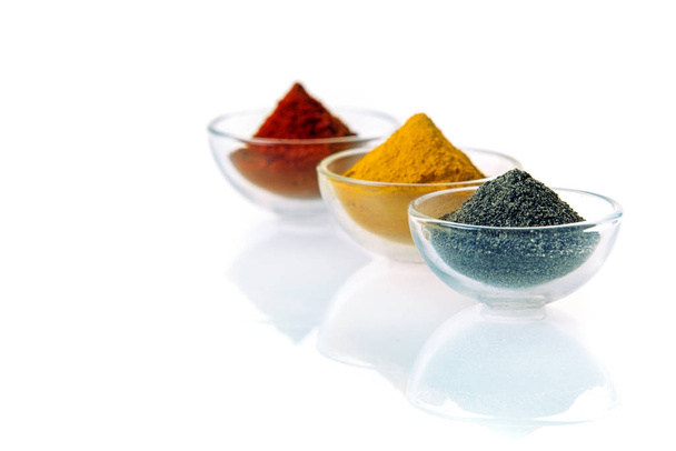 Neat conical heaps of black lava salt, curry and chilli or red pepper powder in clear transparent glass bowls on a white background with reflection and copyspace - Foto, imagen