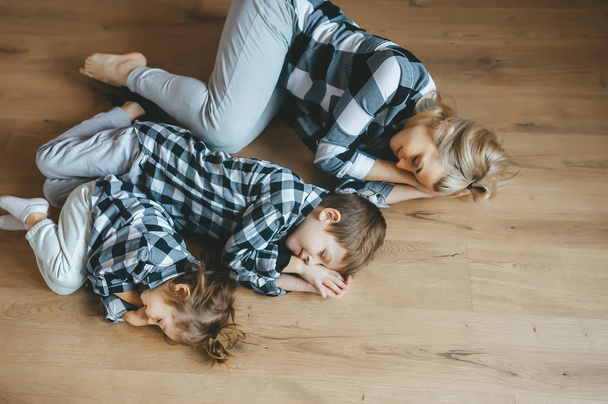 Draufsicht auf Mutter und ihre beiden Kinder in identischer Kleidung, die mit geschlossenen Augen auf dem Boden liegen. Ansicht von oben - Foto, Bild