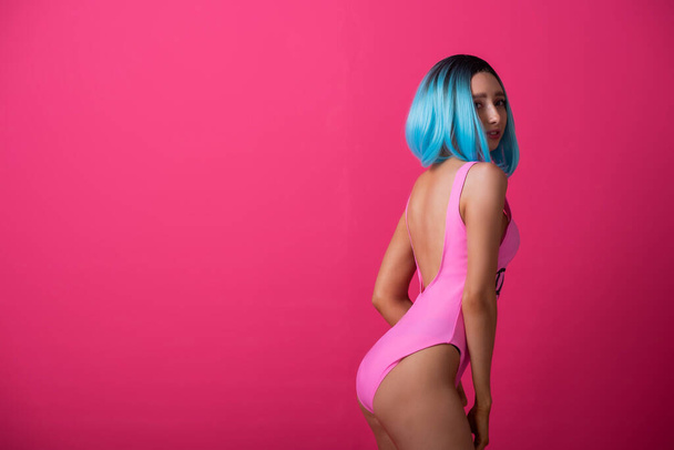 Pretty woman in a pink monokini and blue wig in the studio. Girl with artificial short hair posing in a colored swimsuit. - Foto, Bild
