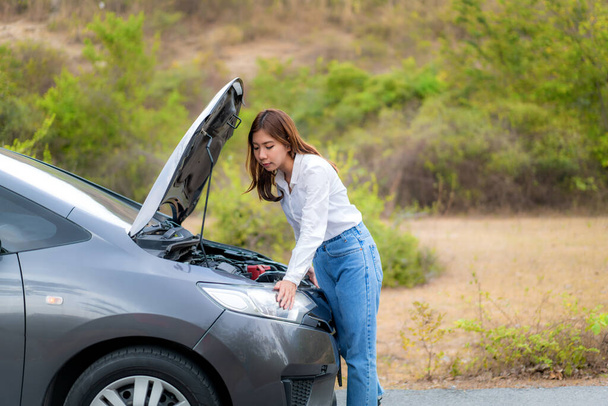Asiatique jeune femme malheureuse inspectant cassé moteur de voiture en face du capot ouvert voiture en panne sur la route de campagne en attente d'un service d'assistance routière. Voiture cassée sur la route pendant le voyage
 - Photo, image