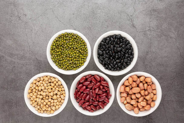 Grains or beans, red bean, black bean, green bean, soybean, peanut in the white bowl placed on the black cement floor. Top view. - Foto, Imagem