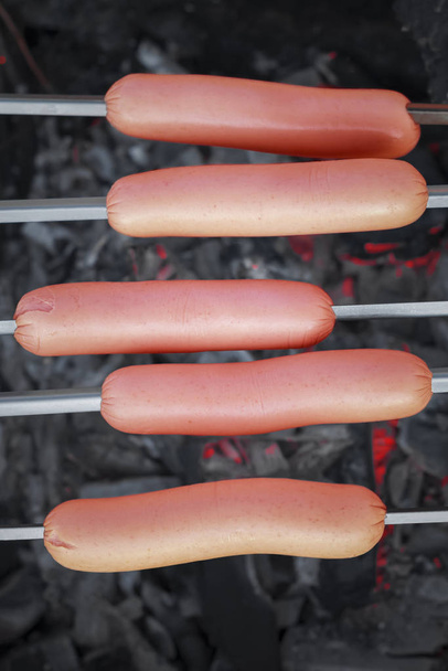 Top view of five fresh sausages on skewers over smoldering hot charcoals - Foto, Bild