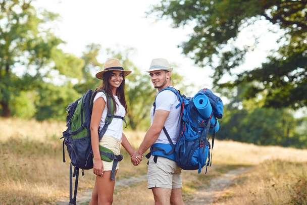 Happy couple of travelers with backpacks hold hands on nature - Foto, afbeelding