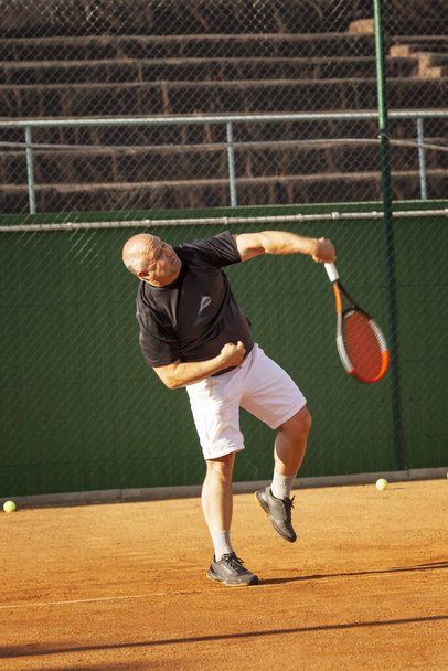 A bald man plays tennis on the court on a sunny day. Health and activity. - Фото, зображення