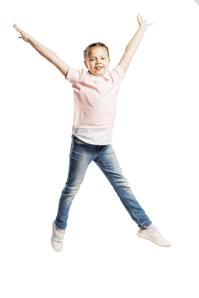 A school-age girl in jeans and a pink sweater is jumping. Isolated on a white background. - Фото, зображення