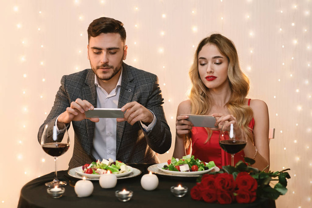 Pareja tomando fotos de su comida durante la cena romántica en el restaurante
 - Foto, imagen
