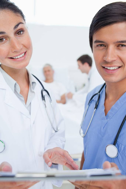 Medico sorridente che tiene una cartellina mentre è accompagnato da un tirocinante mentre si trova di fronte a un medico e un paziente
 - Foto, immagini