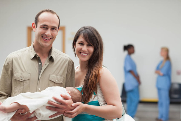 Улыбающаяся пара держит новорожденного ребенка в больнице
 - Фото, изображение
