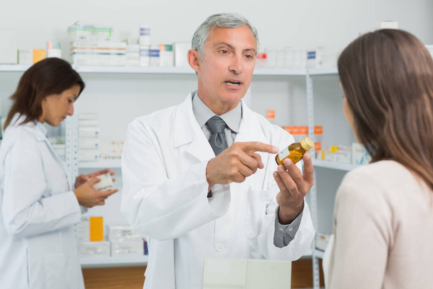 Pharmacist pointing a flask of pills in front of a customer in a pharmacy - Фото, зображення