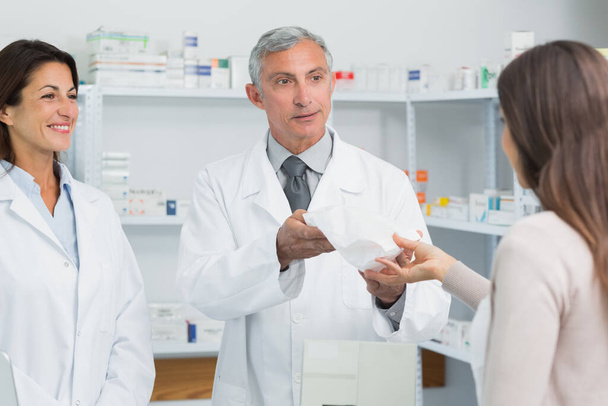 Smiling pharmacist with a colleague in front of a female client in a pharmacy - Foto, Bild