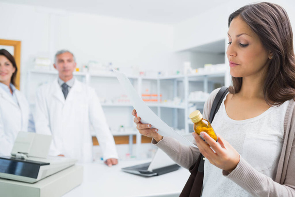 Female client holding a paper and pills while standing in a pharmacy with pharmacists - Fotografie, Obrázek