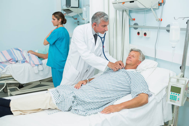 Male doctor auscultating a male patient in a bed ward in a hospital - Fotoğraf, Görsel