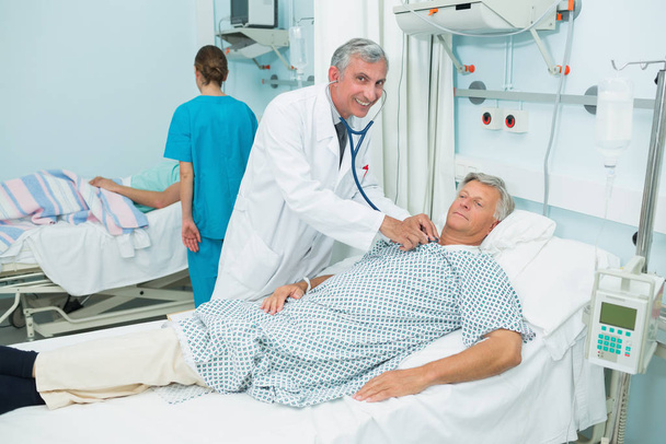 Smiling male doctor auscultating a male patient in a bed ward in a hospital - Fotoğraf, Görsel