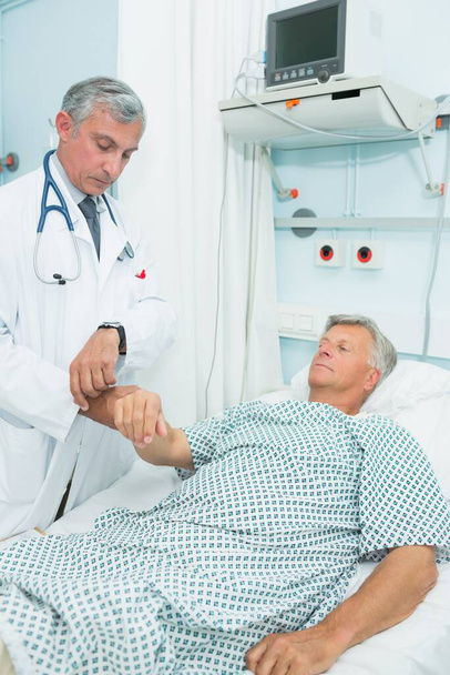 Doctor measuring the pulse of a male patient in a hospital - Fotoğraf, Görsel