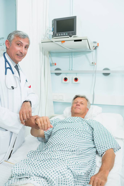 Médecin souriant mesurant le pouls d'un patient masculin dans un hôpital - Photo, image