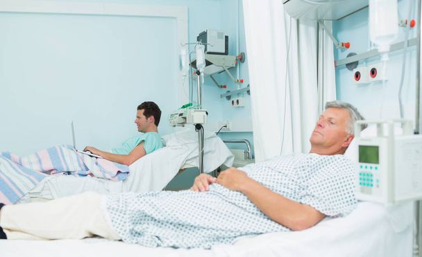 Two male patients lying on hospital beds in a hospital ward - Foto, Imagen