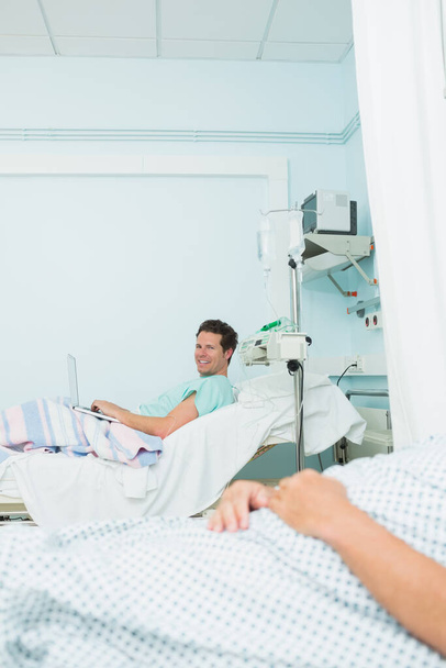 Улыбающийся пациент в больничной палате с другим пациентом в больничной палате - Фото, изображение