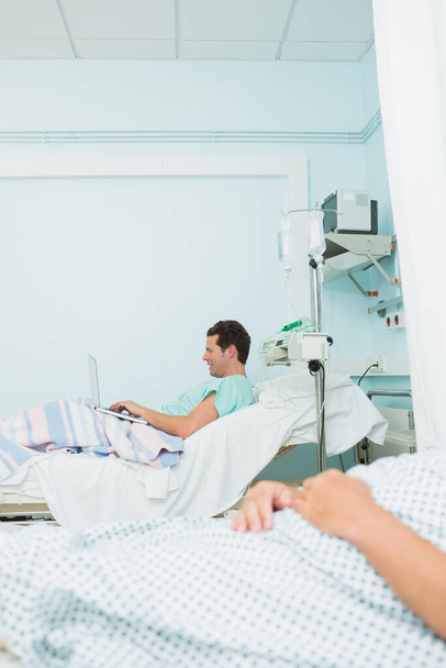 Focus shot of a patient holding a laptop while lying on a bed in a hospital - Valokuva, kuva