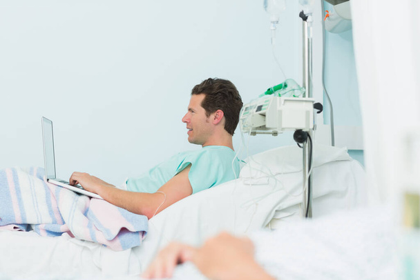 Focus shot of a male patient holding a laptop while lying on a bed in a hospital - Foto, Imagem
