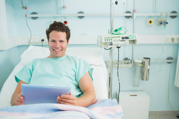 Male patient holding a tactile tablet while lying on a bed in a hospital - Foto, immagini