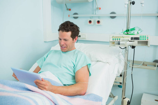 Happy patient holding a tactile tablet while lying on a bed in a hospital - Valokuva, kuva