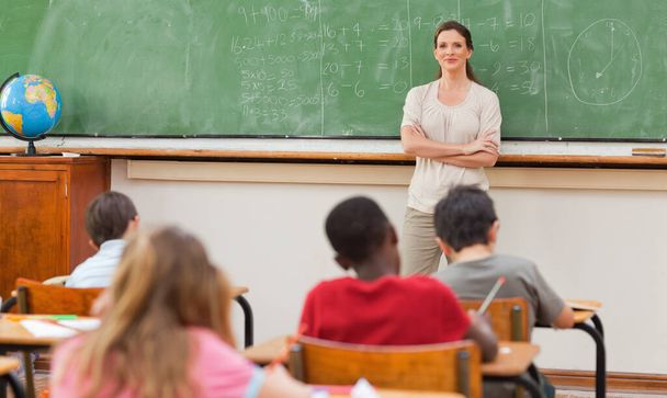 Teacher with arms folded next to blackboard - Foto, Bild