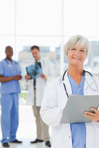 Mature doctor with clipboard and colleagues behind her - Photo, image