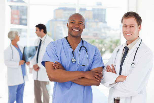 Smiling doctors with arms folded and colleagues behind them - Photo, Image