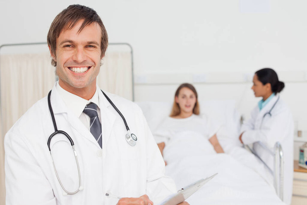 Smiling doctor standing upright in front of a patient and a colleague - Photo, Image