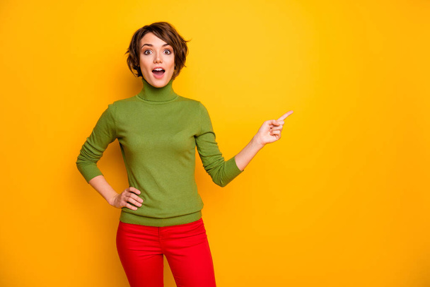 Photo of pretty lady open mouth indicating finger empty space advising black friday low prices store mall wear casual green turtleneck red trousers isolated yellow color background - Foto, Imagen