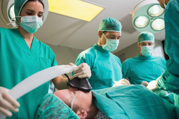 View of a anesthetist holding a while looking at patient in an operating theatre - Foto, Imagen