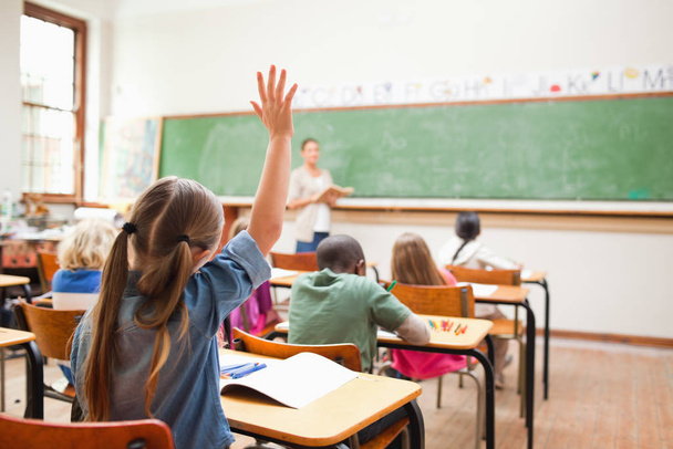 Back view of elementary school student raising her hand - Foto, afbeelding