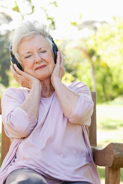 Woman listening to music while holding headphones to her ears - 写真・画像