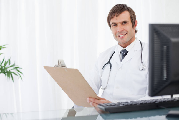Smiling doctor looking at the camera while holding his clipboard - Foto, Bild