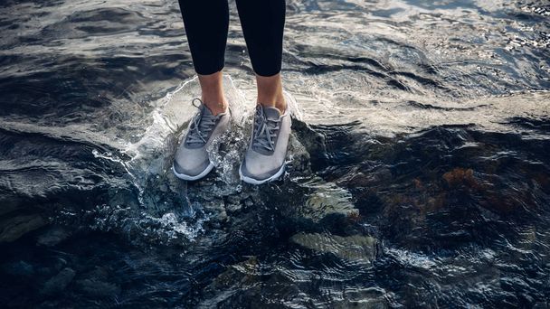 Onherkenbaar meisje in sneakers staat op het water, uitzicht op de benen, close-up. Religie klimaat business sport vrijheid concept - Foto, afbeelding