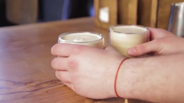 Barista postavil šálky vařeného mléka na stůl v kavárně. Mužské ruce položí šálky na stůl a návštěvník je vezme za ruku. - Záběry, video