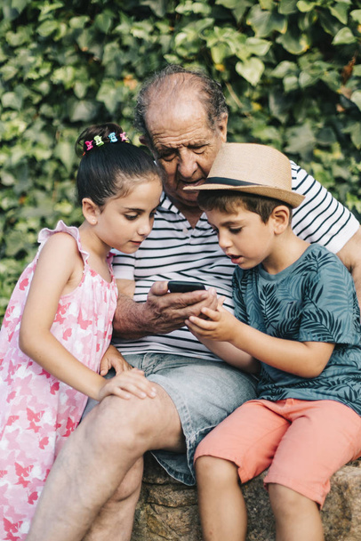 Grootvader en kleinkinderen spelen met een mobiele telefoon - Foto, afbeelding