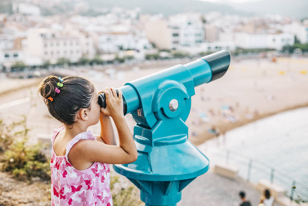 Девушка смотрит на пляж через телескоп
  - Фото, изображение