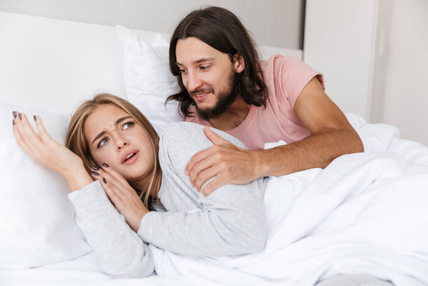 Beautiful young couple laying in bed at home, smiling man - Φωτογραφία, εικόνα