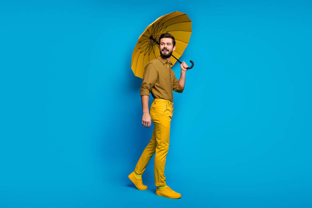 Full size photo of cheerful guy enjoy spring rainy weather hold bright umbrella look good copyspace wear shoes isolated over blue color background - Foto, Bild