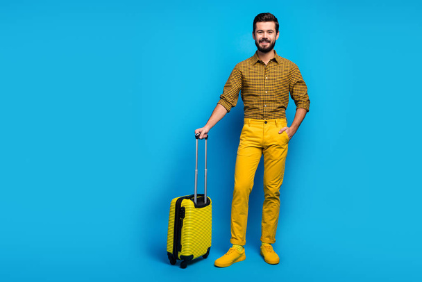 Full length photo of positive cheerful guy have big bright bag trolley enjoy tourism weekend wear good look trendy clothing gumshoes isolated over blue color background - Foto, Imagem