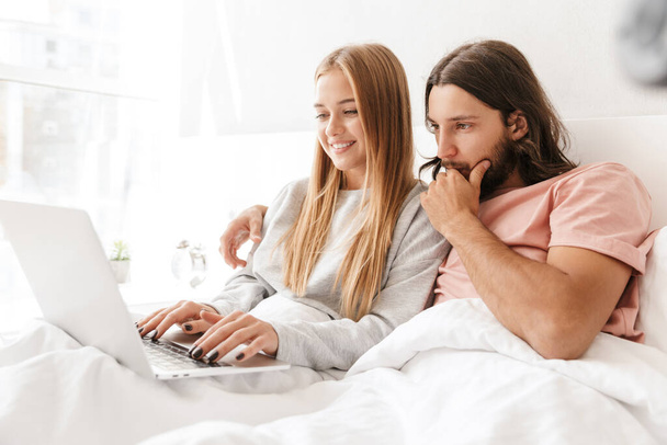 Loving couple in bed using laptop computer at home. - Фото, изображение