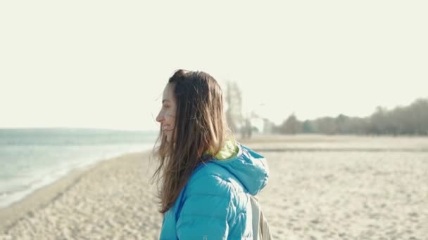 Güneşli bir günde kumlu sahilde yürüyen bir kadın saçlarını savuruyor. - Video, Çekim
